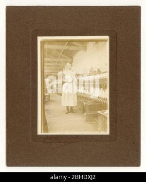 Early 1900's photograph of Lancashire cotton spinner, standing next to a spinning mule  in a cotton mill, wearing clogs, Radcliffe, Lancashire, U.K. circa 1915