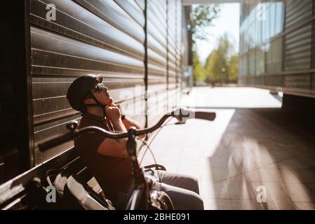 A handsome young caucasian man sits on a bench next to his bike Stock Photo