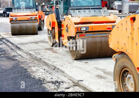 Large and heavy orange vibratory rollers stand on the roadway awaiting work. Stock Photo
