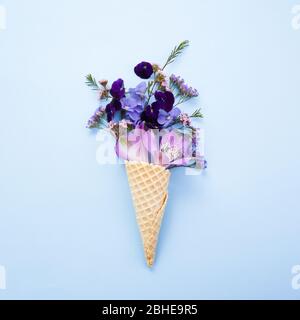 Purple flowers in waffles in flat style on blue background. Flatlay, top view. Birthday, spring background. Stock Photo