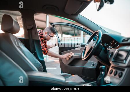 Young man carefully cleaning the interior of his car with a rag. Stock Photo