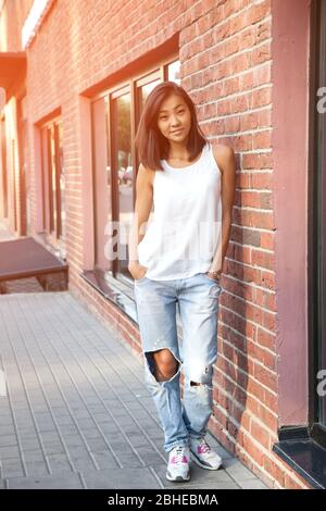 Beautiful Asian happy girl in sports style stands near the city brick wall Stock Photo