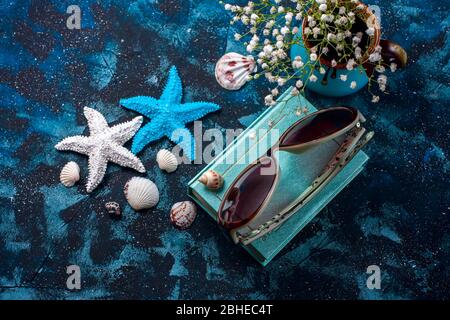 Beach accessories. Seashells, sunglasses and starfish on a dark blue background. With copy space. Selective focus Stock Photo