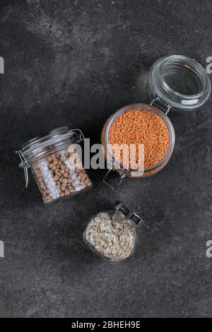 Various uncooked cereals, grains for healthy cooking in glass jars on dark slate table, background. Clean eating, vegan, balanced dieting food concept Stock Photo