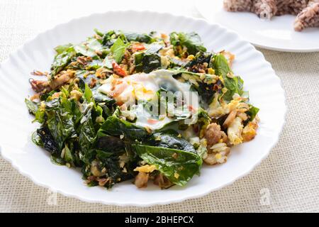 A white plate of delicious Stir-Fried Baegu Leaves or Melinjo with Eggs, served with steamed rice. Stock Photo