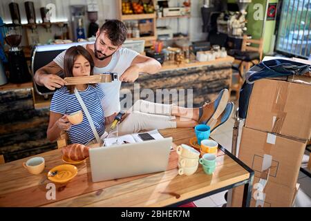 young man is putting a tape across woman's mouth, joking as she talk too much. young couple joking in new  unopened cafe of their own. Starting new bu Stock Photo