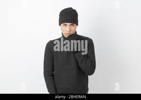 Young handsome asian man wearing grey sweater and beanie trembling, shaking from cold wind, freezing on white background. Stock Photo