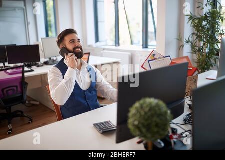 young business man alone in the office, working overtime, talking on a phone, receiving good news. Success, good news, business concept Stock Photo