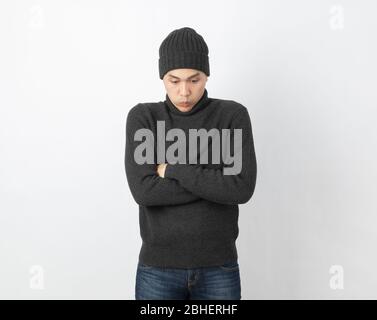 Young handsome asian man wearing grey sweater and beanie hugging herself and trembling, shaking from cold wind, freezing on white background. Stock Photo