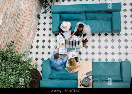 Business, teamwork concept. Group of multiethnical business colleagues sitting on blue sofas, discussing the charts and graphs showing the results of Stock Photo