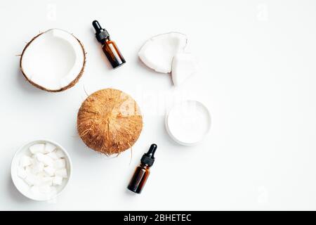 Flat lay composition with coconut essential oil bottles, moisturizing face cream lotion and coconuts on white background. Top view SPA natural organic Stock Photo