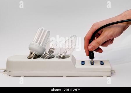 Power strip with three light bulbs of different type, white background and an hand holding a plug Stock Photo