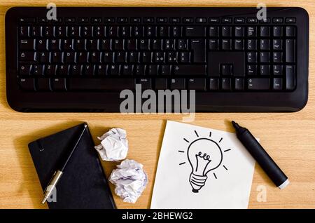 computer keyboard on a desk with agenda, marker pen, crumpled sheets and a white sheet with a a light bulb drawing Stock Photo