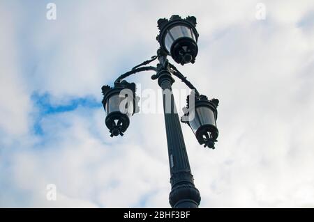 Grey metal lamppost with three figured glass lanterns, cloudy sky. View from the bottom to the top Stock Photo