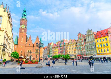 Wroclaw, Poland, May 7, 2019: Row of colorful buildings with multicolored facade, Old Town Hall and people walking on Rynek Market Square with cobblestone street in old historical city centre