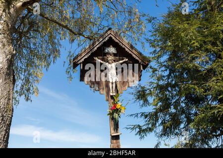 A common sight when hiking through Bavaria: Jesus on the cross. White sculpture, carved out of wood. With small roof as protection. Stock Photo