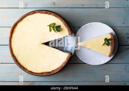 Plane round classic New York cheesecake and his slice with sprig of mint on a plate on a wooden table. The concept of bakery and sweet cakes desserts