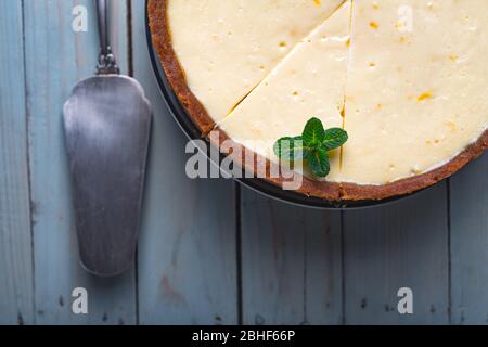 Plane round classic New York cheesecake and his slice with sprig of mint on a plate on a wooden table. The concept of bakery and sweet cakes desserts Stock Photo