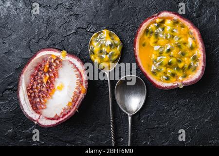 Slised passion fruit with silver spoons on black concrete background. Food photography Stock Photo
