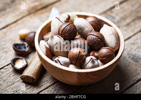 Dried mixed nuts in wooden bowl closeup. Macadamia, Pecan and Brazil nuts with knife on wooden table. Studio macro shoot. Stock Photo