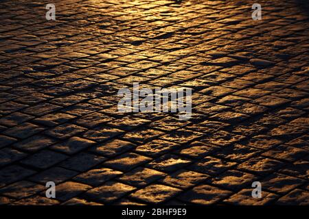 Stone road in the street of old town. Top layer of a roadway in a historic city center. Cobblestone pavement of  in the rays of the evening sun light. Stock Photo