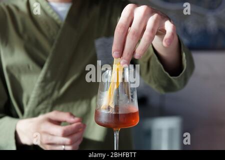 Male bartender is adding lemon zest to cocktail in wine glass Stock Photo