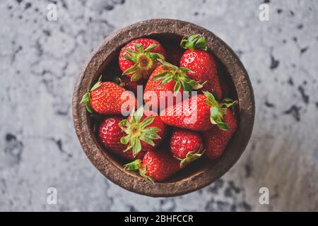 Heap of fresh strawberries in ceramic bowl on cement background Stock Photo