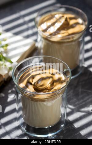 Dalgona Coffee in transparent glasses on a windowsill illuminated by sunlight. Stock Photo