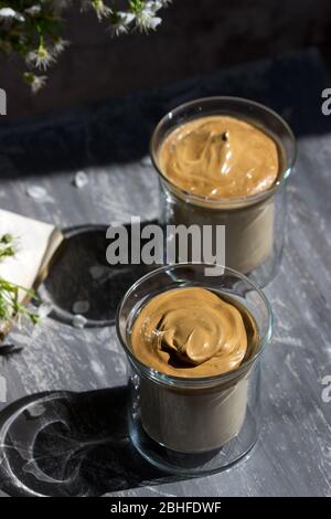 Dalgona Coffee in transparent glasses and a book on a sunlit table. Stock Photo