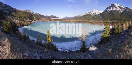 Frozen Ice Covered Rocky Mountain Gap Lake Bow Valley Scenic Panoramic Landscape View.  Distant Alberta Foothills Canadian Rockies Banff National Park Stock Photo