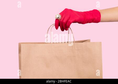 Womans hand in a rubber glove holding paper bag on pink background Stock Photo
