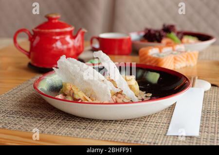 Fried shrimps in wasabi sauce, maki rolls and tea kettle on restaurant table Stock Photo