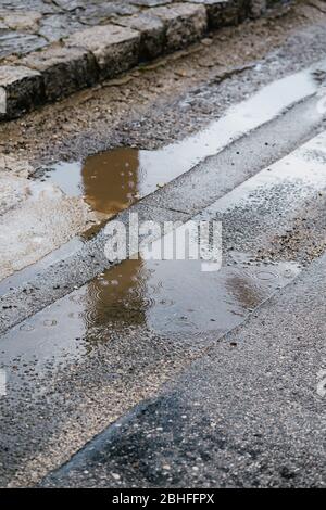 Raindrops in a puddle on the pavement. Circles on the water from a drop of rain in a puddle on the asphalt Stock Photo