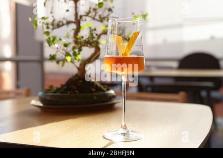 Japanese style cocktail with lemon zest in wineglass, bonsai tree, sunlight Stock Photo