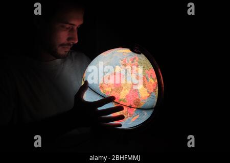 a man looking at a Rotating World Globe Earth Lamp light Illuminated Desk Map Geography in the dark night with it face illuminated Stock Photo