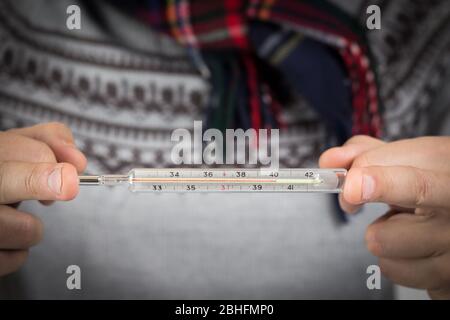 traditional mercury thermometer in man hands showing high body temperature 40 degree because of illness influenza or cold Stock Photo