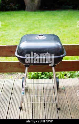 Full view of small compact barbecue grill with charcoal placed on patio with garden view Stock Photo