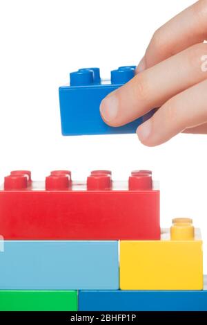 Close up of a kid’s hand stacking toy building blocks, isolated on a white background Stock Photo