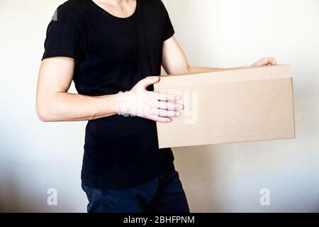 Close up delivery man hands in gloves hold cardboard box. Delyvery and volunteering during coronavirus pandemic quarantine. Stock Photo