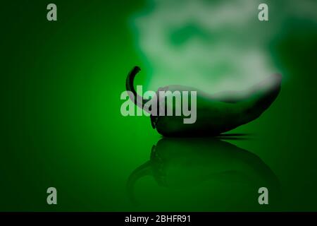 Shot of fresh green chili isolated on a green colored background with some smoke coming out of it indicating the hotness of chili. Stock Photo