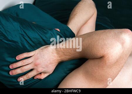 Handsome young male insomniac covering his head and ears trying to block out the sound with a pillow as he kept awake by loud noises Stock Photo