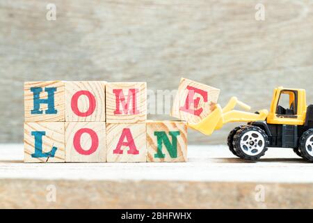 Toy bulldozer hold letter block e to complete word home loan to on wood background Stock Photo