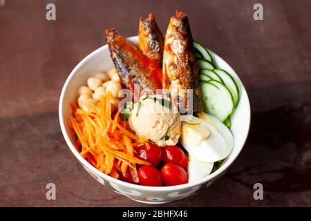 Colorful salad in white china bowl with sardines, carrots, cucumber, boiled eggs, cherry tomato and chickpea Stock Photo