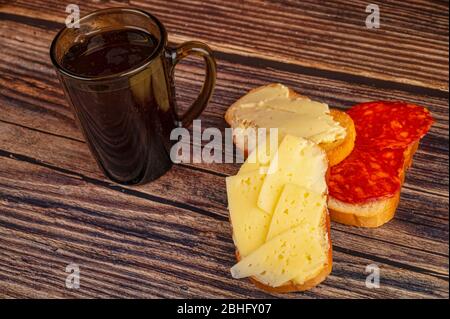 fresh wheat toast with butter, sausage and cheese and a mug of tea on a wooden background. Close up Stock Photo