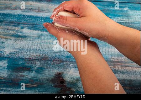 Someone is soaping their hands with a piece of toilet soap on a wooden background. Close up. Washing hands with soap is a prevention of COVID-19 infec Stock Photo