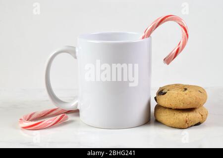 11 ounce white coffee cup resting merrily on a marble tabletop surrounded by candy canes and chocolate chip cookies. Stock Photo