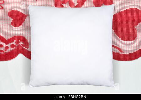 Square white throw pillow resting romantically on a Valentine’s table runner with hearts. Stock Photo