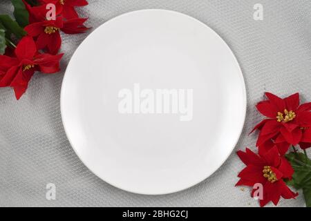 White plate resting merrily on a gray tablecloth surrounded by festive Christmas Poinsettias. Stock Photo