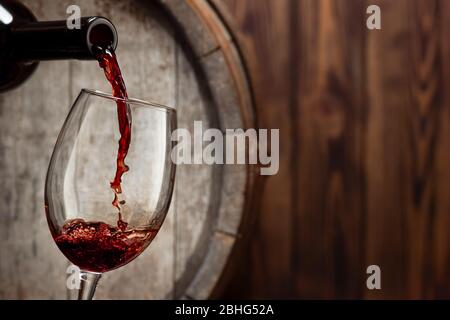 red wine pouring from bottle into glass with old wooden barrel as background Stock Photo