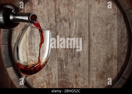 red wine pouring from bottle into glass with old wooden barrel as background Stock Photo